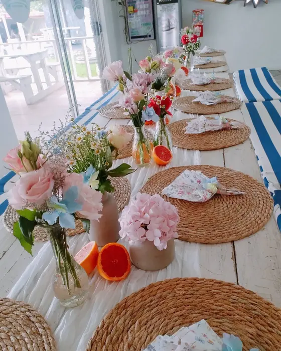 A white table with pink roses and carnations in small vases, grapefruit halves and woven placemats.