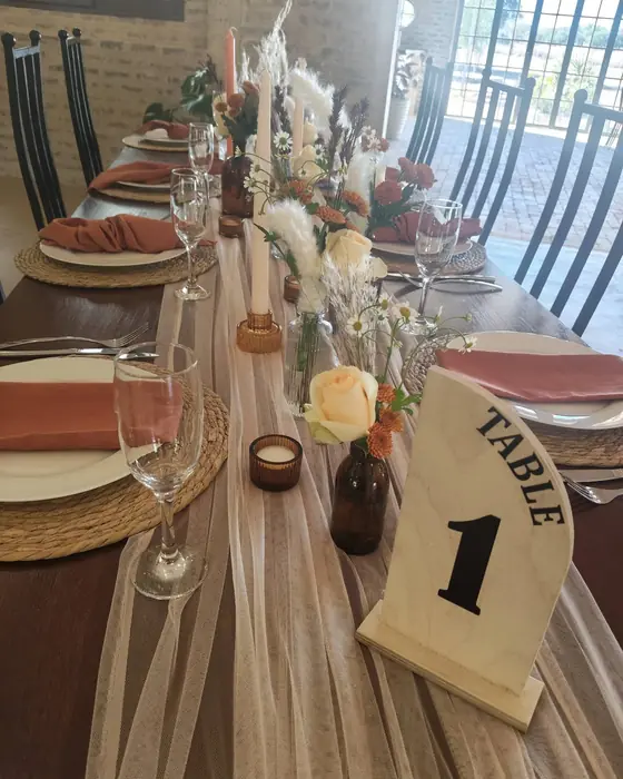 A tulle runner with dried flowers in amber bottles, a peach rose and a timber table number one.