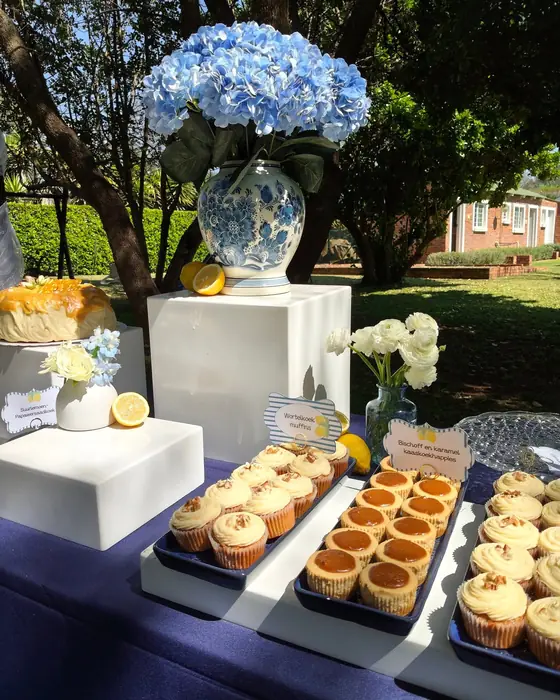A dessert table with blue hydrangeas in a ginger jar, cupcakes and lemon tarts on a navy cloth.