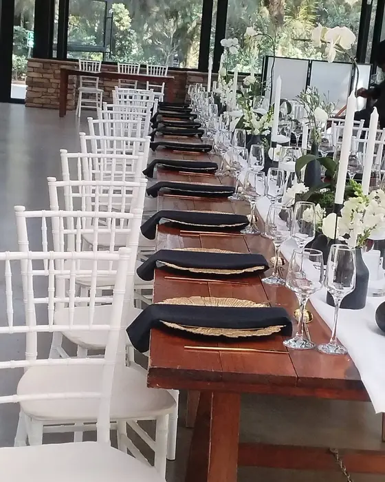 A long table with navy napkins, white chairs and white flowers in a bright venue.