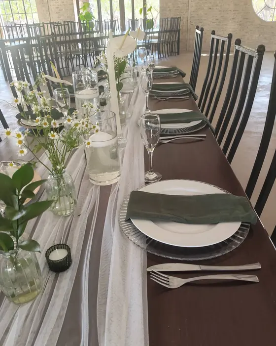 A dark timber table with an ivory chiffon runner, single white flowers in bud vases and sage green napkins.