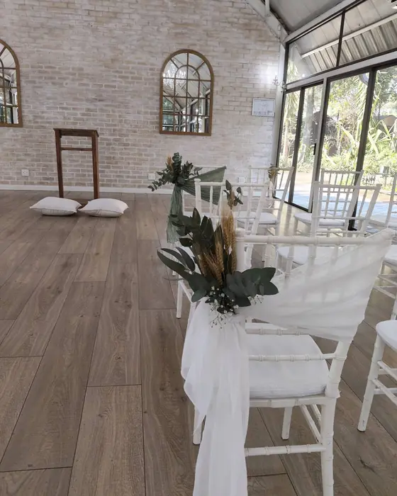 A ceremony aisle with white chairs tied with chiffon and a posy of dried flowers and greenery.