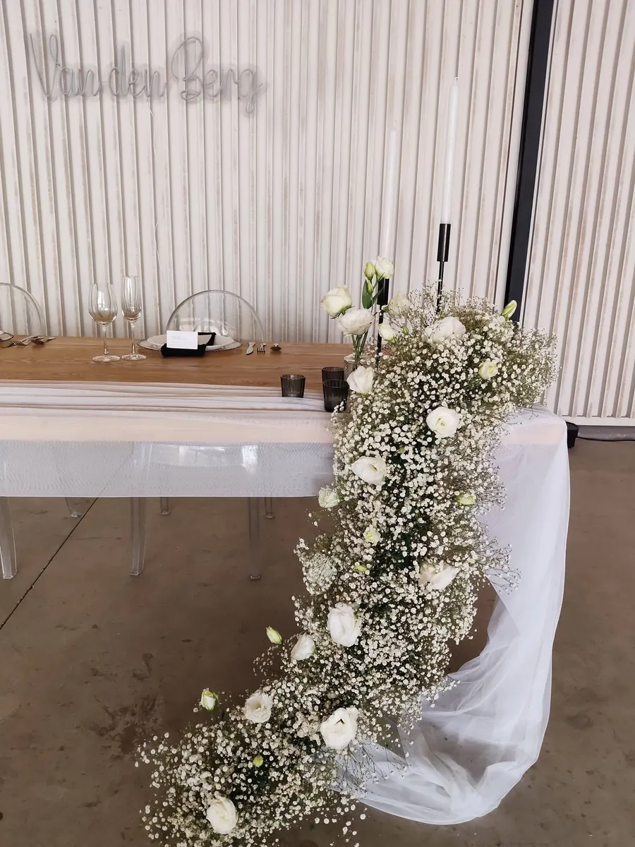A cascade of white roses and baby's breath spilling over the end of a head table onto a tulle drape.